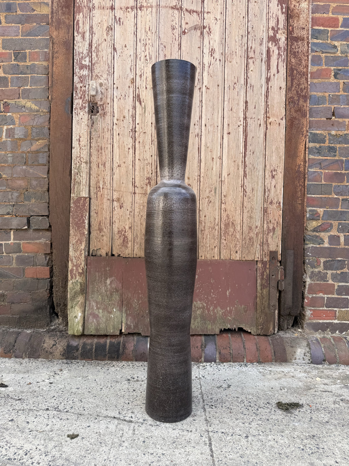 Grande pièce verticale réalisée en Faïence Normande Noire FA100 devant une porte ancienne de la manufacture